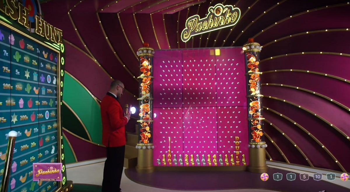 The host releases a ball onto a wall with physical pegs, causing the ball to bounce randomly and hit different pegs before ultimately landing on a prize at the bottom of the screen.